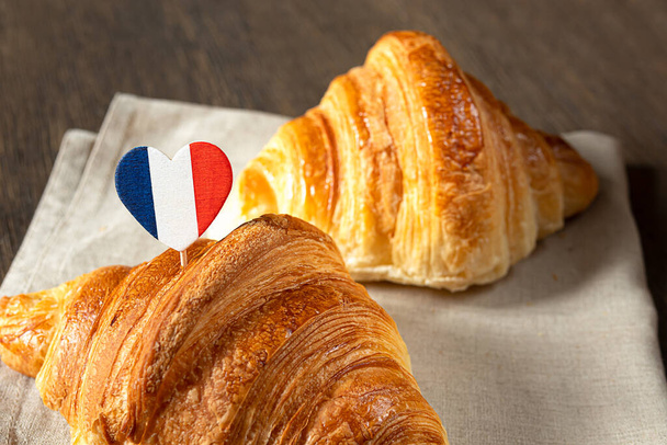 Zwei frische französische Croissants und ein Herz in den Farben der französischen Flagge auf einem Tisch - Foto, Bild