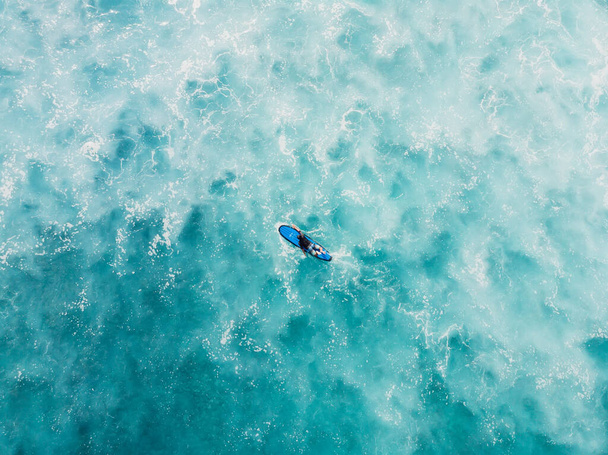 Aerial view of surfer on longboard in blue ocean with foam. Top view - Foto, Bild