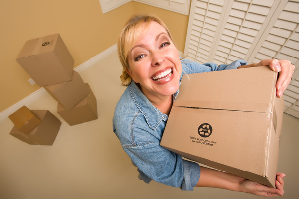Femme excitée tenant des boîtes mobiles dans une pièce vide prise avec un objectif extrême grand angle
. - Photo, image
