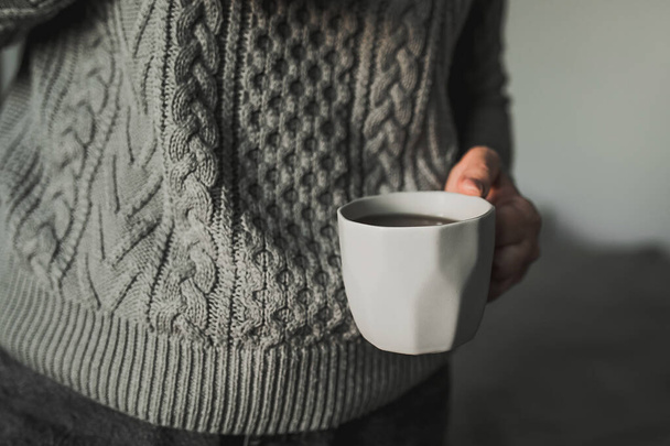 Γυναίκα σε ζεστό γκρι πλεκτό πουλόβερ κρατώντας κούπα καφέ, τσάι. Χειμωνιάτικο πρωινό - Φωτογραφία, εικόνα