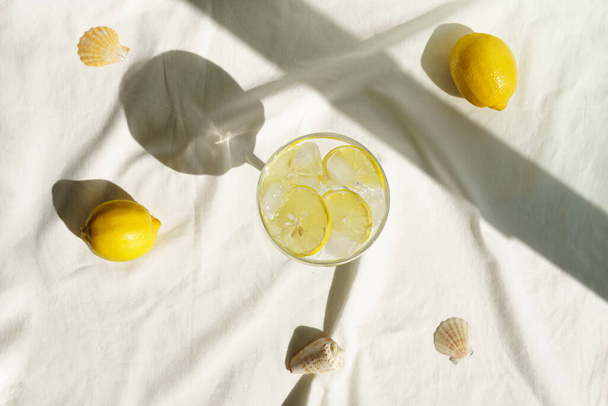 Limonlu ve güneş gölgeli kokteyl ya da su. Bej kumaşın arka planında. Üst görünüm - Fotoğraf, Görsel