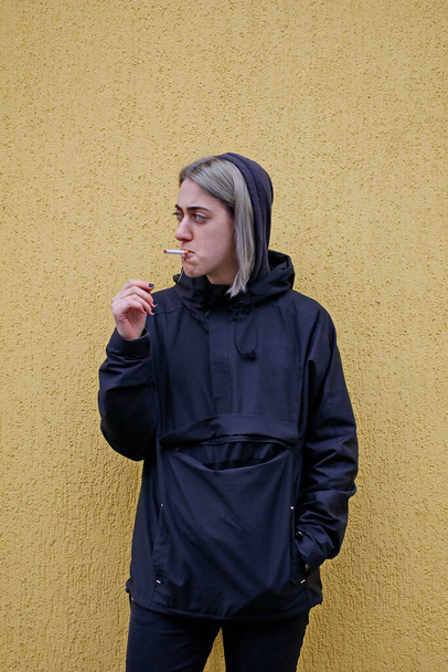 Η κοπέλα με τα ασημένια μαλλιά ντυμένη στα μαύρα καπνίζει ένα τσιγάρο. - Φωτογραφία, εικόνα