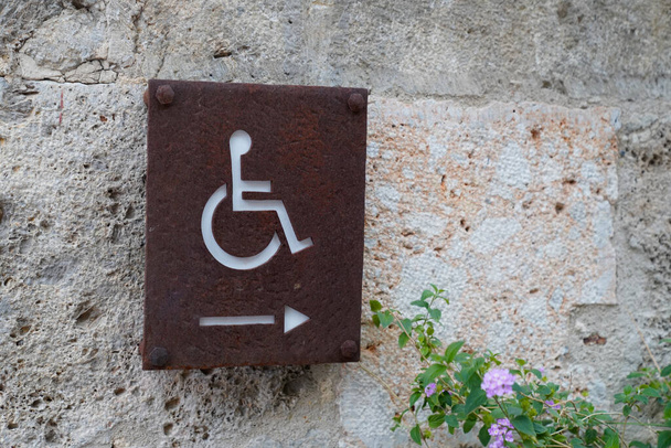 Вывеска со стрелкой для инвалидов с логотипом инвалидной коляски, указывающая сбоку на стене подъезда магазина пиктограмма на улице магазина - Фото, изображение