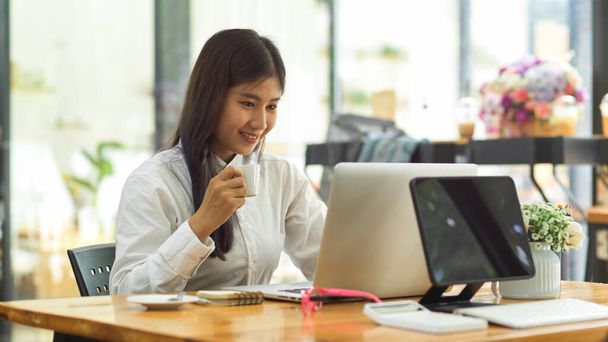 Happy young female worker working with laptop and supplies in co-working space  - 写真・画像