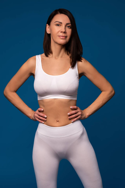 Stolze selbstbewusste Frau in weißer Sportbekleidung auf blauem Hintergrund - Foto, Bild