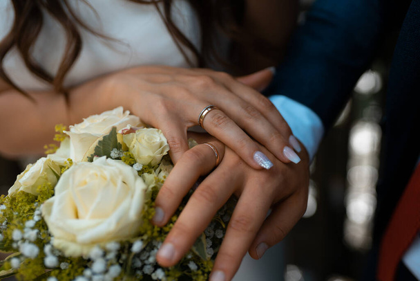The hands of an unrecognizable bride on a bouquet of bridal flowers wearing a wedding ring - Foto, imagen