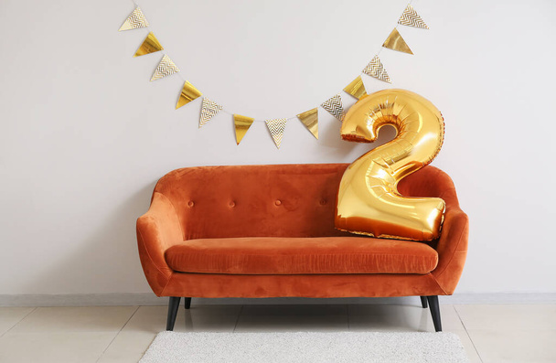 Balloon in shape of figure 2 on sofa near light wall decorated for birthday - Photo, Image