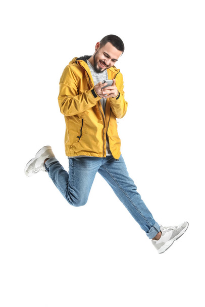 Jumping young man with mobile phone on white background - Fotoğraf, Görsel