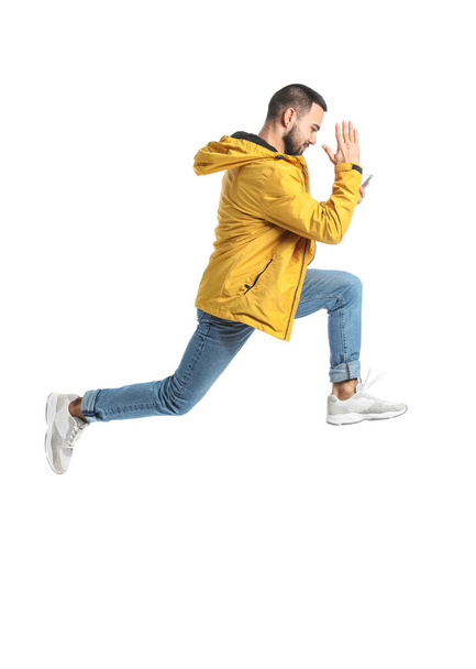 Jumping young man with mobile phone on white background - Fotó, kép