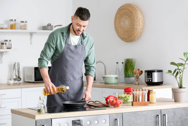 Человек льет подсолнечное масло на сковородку на кухне - Фото, изображение
