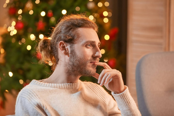 Handsome man sitting on sofa at home on Christmas eve - Foto, imagen