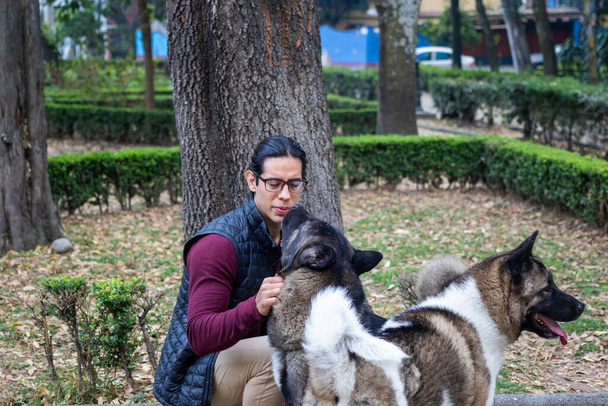 Young muscular hispanic man holding and petting his dogs in the park - Valokuva, kuva