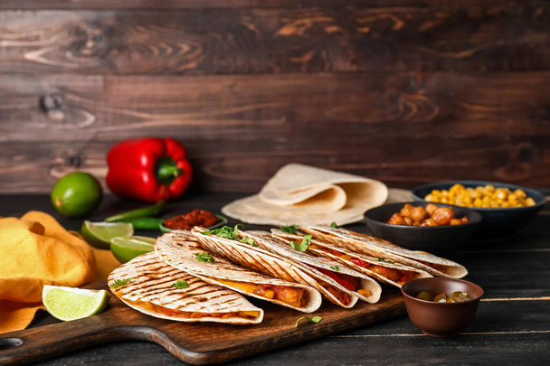 Board with tasty quesadillas on wooden background - Photo, image