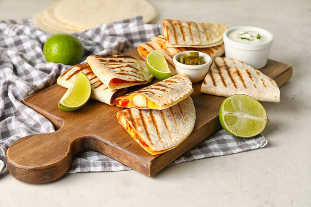 Tafel mit leckeren Quesadillas, Limetten, Sauce und eingelegten Jalapenos auf hellem Hintergrund - Foto, Bild