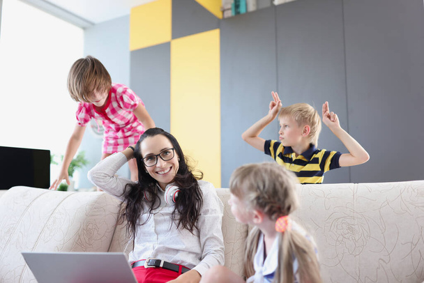 Woman sitting on sofa with laptop next to small children at home - Photo, Image