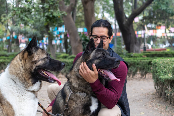 Young muscular hispanic man holding and petting his dogs in the park - Foto, Bild