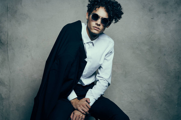 trendy guy with curly hair indoors on a fabric background and a jacket on the shoulder - Photo, Image