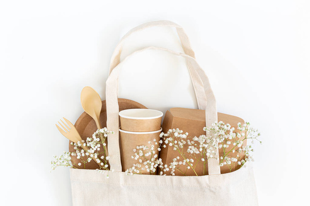 Eco tableware and gypsophila flowers in a shopping bag on a white background. - Photo, image