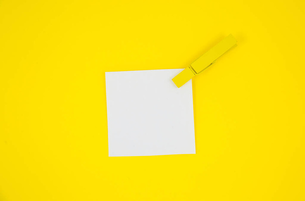 Weiße Aufkleber mit gelben Holzklammern auf der To-Do-Liste. Großaufnahme des Mahnzettels auf gelbem Hintergrund. Kopierraum. Minimalismus, originelles und kreatives Foto. - Foto, Bild