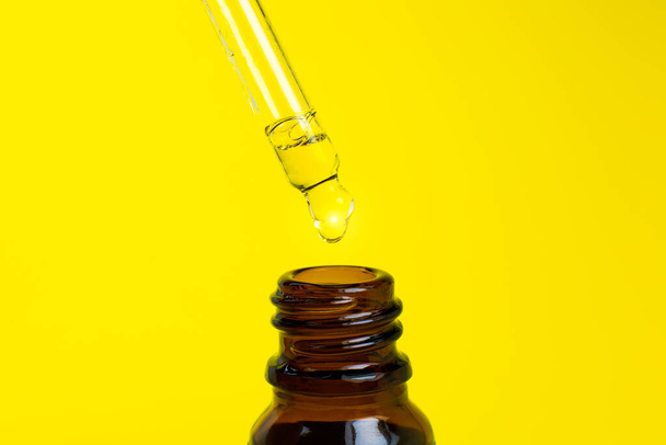 Bottle of cosmetic oil with a pipette on a yellow background. Close up liquid drop dripping. Beauty, medicine and  health care concept. Macro photo. Natural, eco cosmetics. - Photo, Image