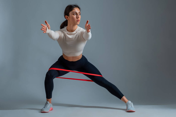 Woman performing resistance band side lunges on grey background - Photo, Image
