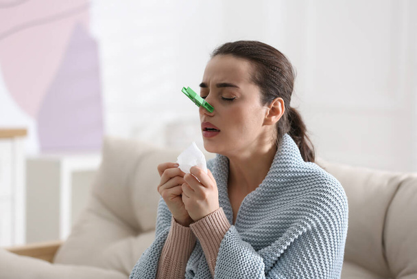 Young woman with clothespin suffering from runny nose in living room - Foto, immagini