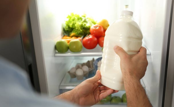 Man putting gallon of milk into refrigerator indoors, closeup - Foto, Imagen