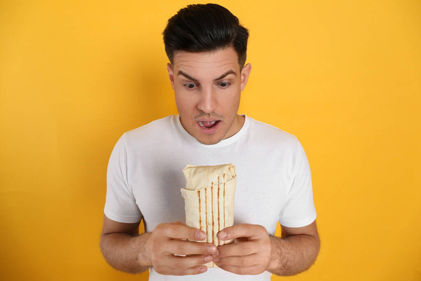 Emotional man with delicious shawarma on yellow background - Фото, зображення