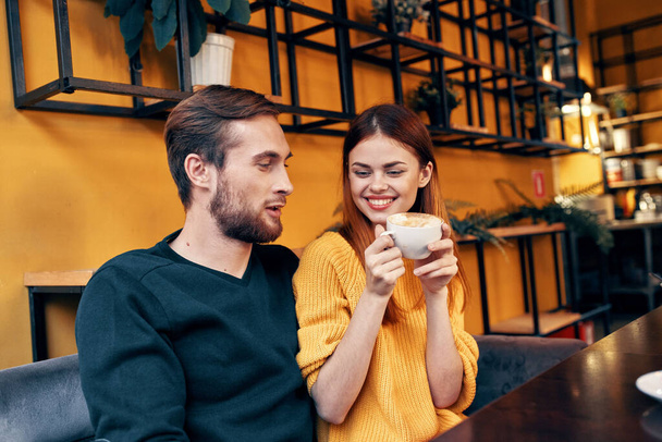 μια γυναίκα ερωτευμένη με ένα φλιτζάνι καφέ και έναν ευτυχισμένο άντρα σε ένα τραπέζι σε ένα καφέ εσωτερική επικοινωνία φίλων - Φωτογραφία, εικόνα