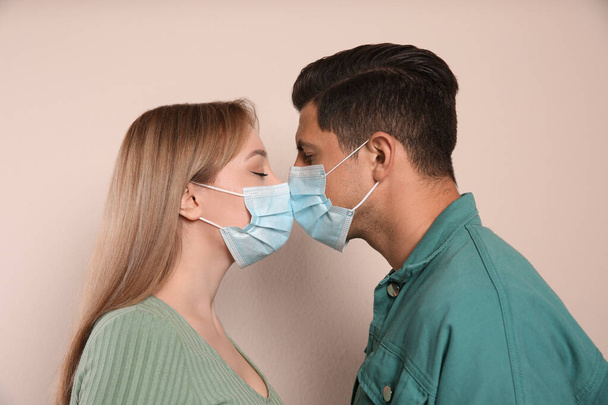 Couple in medical masks trying to kiss on beige background - Fotografie, Obrázek