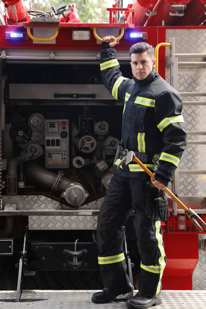 Portrait of firefighter in uniform with entry tool near fire truck outdoors - Foto, afbeelding