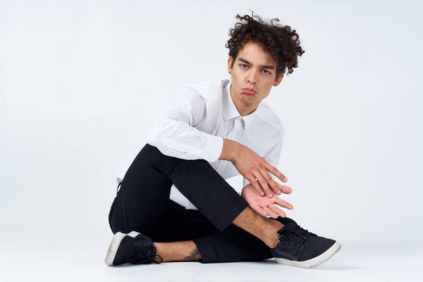 Молодой человек с вьющимися волосами сидит на полу со скрещенными ногами - Фото, изображение