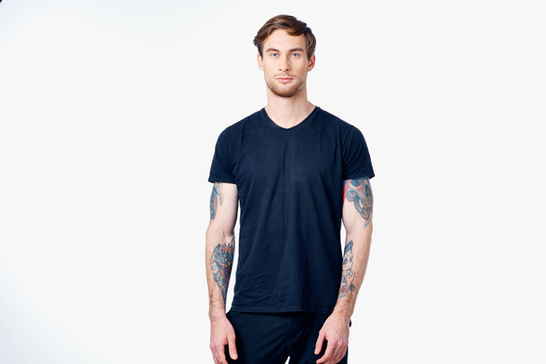 muscular man in a blue t-shirt with tattoos on his arms on a light background cropped view - Photo, image