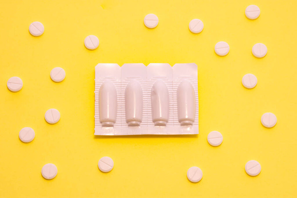 Trattamento con farmaci sotto forma di supposte malattie della sfera urinaria. L'imballaggio delle candele medicinali è su sfondo giallo - colore dell'urologia - circondato da pillole bianche - Foto, immagini