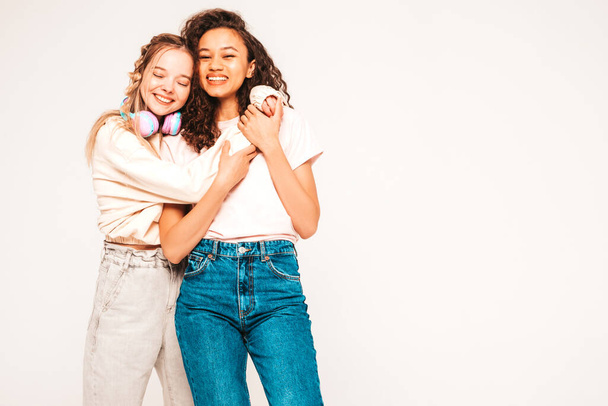 Two young beautiful smiling international hipster female in trendy summer clothes.Sexy carefree women posing on grey background in studio.Positive models having fun.Concept of friendship - Foto, Bild