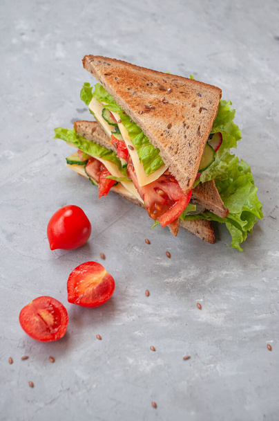 Lahodný sendvič s čerstvými listy salátu, rajčaty, okurkami a sýrem na šedém podkladu stolu. - Fotografie, Obrázek