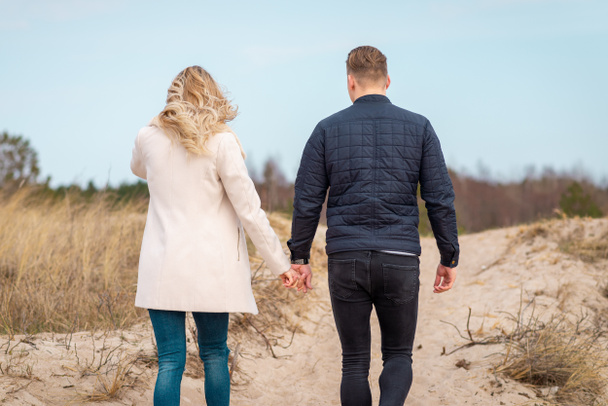 Ein junges Paar, das auf Sanddünen spaziert, hielt Händchen.In der Ferne der Wald.. - Foto, Bild