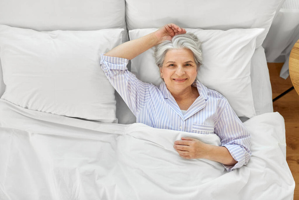 smiling senior woman lying in bed at home bedroom - Fotó, kép