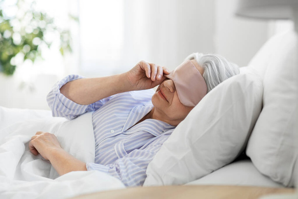 senior woman with eye sleeping mask in bed at home - Foto, Imagem
