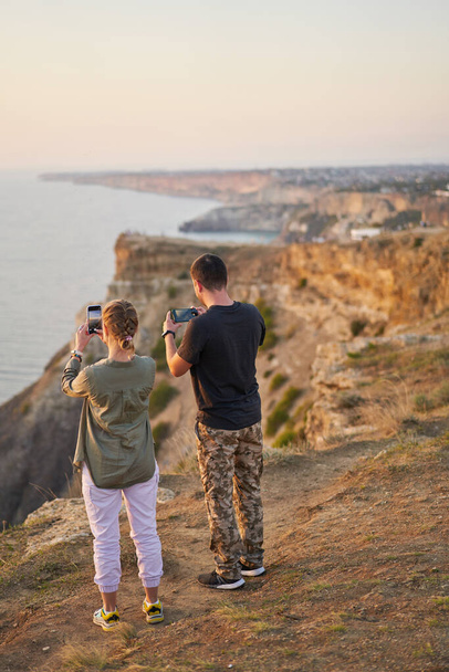 Echtpaar verblijft op de rots, maakt foto 's en geniet van het uitzicht op zee en de frisse lucht. - Foto, afbeelding