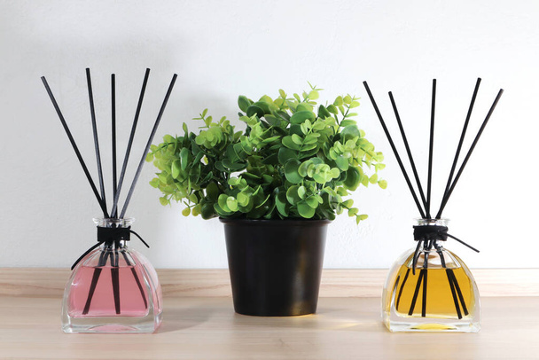 Luxury aroma scented reeds sticks diffuser glass bottles are displayed  on the wooden table with a plant flower pot in the white bedroom background white cement wall - Photo, Image