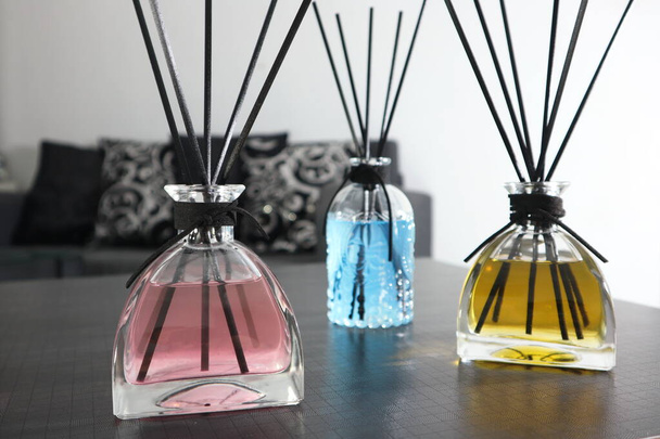 luxury glass aroma reed diffuser bottle with blue , orange and pink colour oil are decorated on the grey table in the white living room of the hotel resort during summer holiday with happy family - Photo, Image