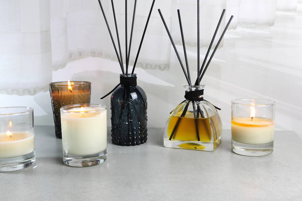 luxusní pěkné skleněné svíčky a aroma pokoj osvěžovač rákosí difuzor tyčinky jsou zobrazeny na šedém stole s bílým závěsem pozadí v ložnici - Fotografie, Obrázek