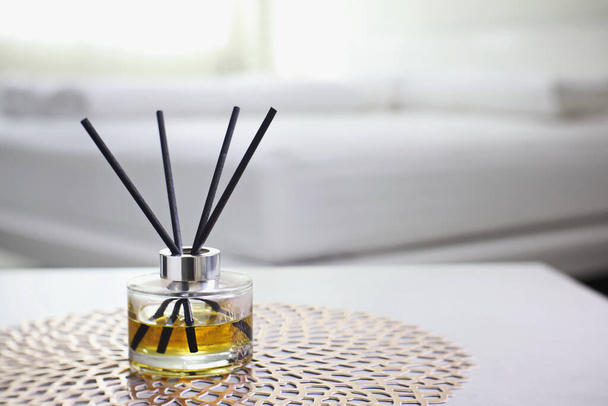 luxury aromatic scent glass of reed diffuser is used as room freshener on the grey table in the white bedroom near the sunlight from the window curtain of the resort hotel in Thailand during summer - Foto, Imagem