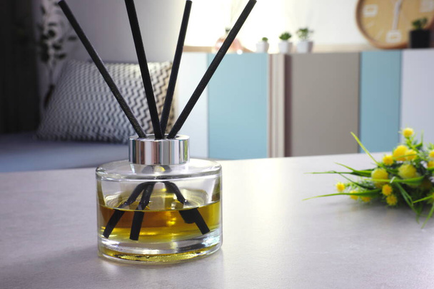 stylowe aromatyczne butelki szklane dyfuzor trzciny z kwiatem i małą rośliną są wyświetlane na szarym stole w sypialni - Zdjęcie, obraz