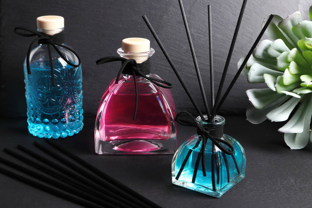luksusowy szklany aromat butelka dyfuzor trzciny z kolorowy niebieski i różowy kolor olejek są wyświetlane na czarnym kamiennym stole z tłem czarnego betonu ściany w ciemnym pokoju łóżko - Zdjęcie, obraz