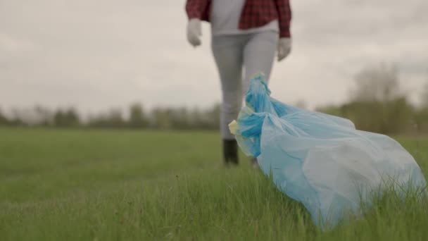 Um homem carrega lixo em sacos de lixo na grama verde, coleta e descarte de resíduos desnecessários, uma mulher em luvas para o trabalho de limpeza, ajudar a proteger o meio ambiente planetas, terra limpa - Filmagem, Vídeo