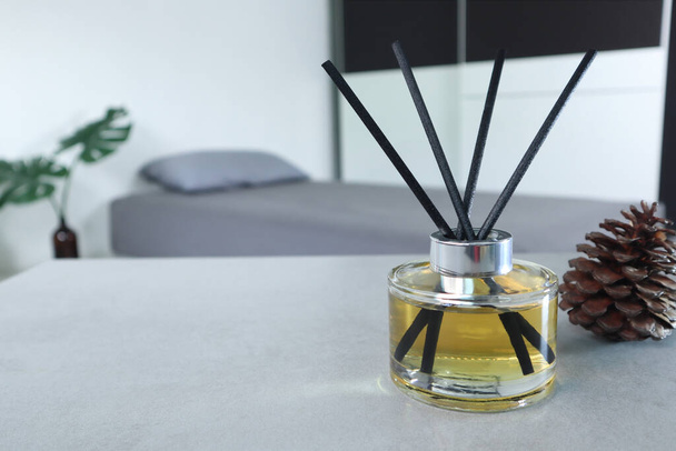 luxuriöse aromatische Duftgläser aus Schilf dienen als Raumerfrischer auf dem grauen Tisch im Schlafzimmer mit Tannenzapfen im Hintergrund des grauen Bettes am Morgen - Foto, Bild