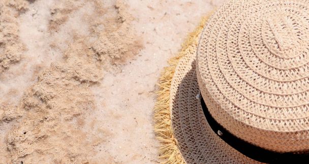 slaměný klobouk leží na slaném bílém písku. Koncept cestování  - Fotografie, Obrázek