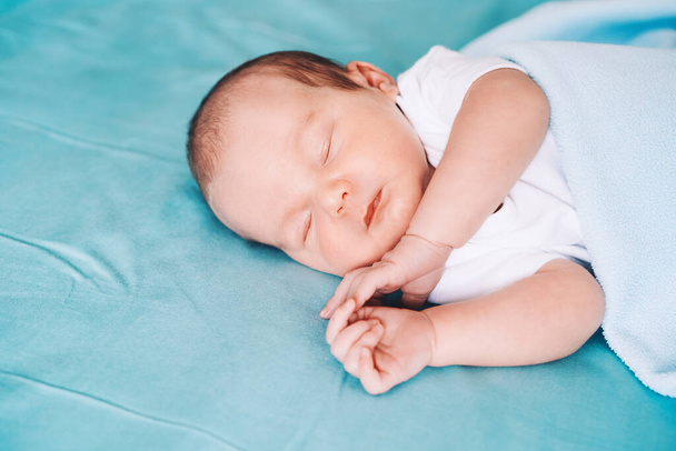 Newborn baby sleep at first days of life. Portrait of new born child boy one week old sleeping peacefully in crib in cloth background. - Zdjęcie, obraz